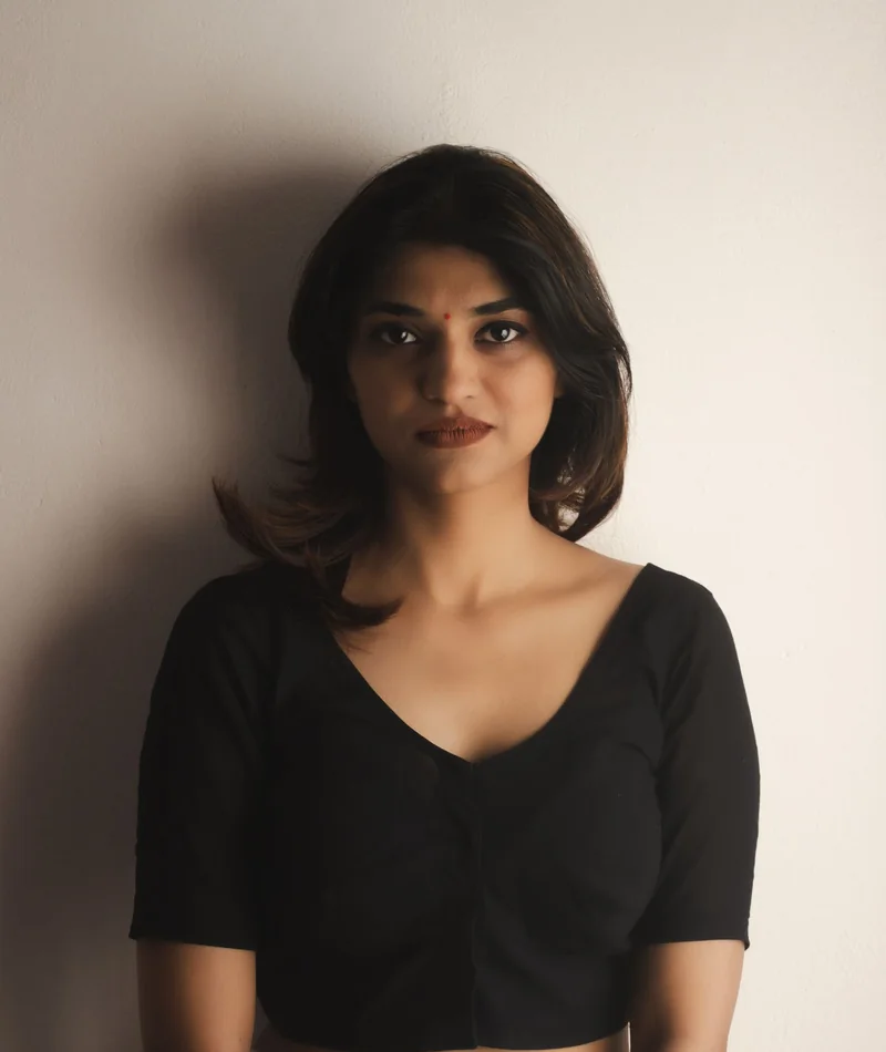 Indian woman with softly styled dark hair against a warm stone wall