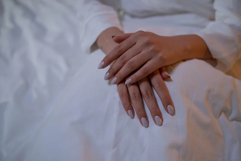 Hands with a subtle nude manicure resting on ivory fabric